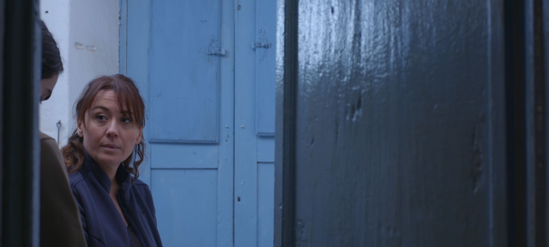 A mother in a room, watching her son hidden by the doorframe